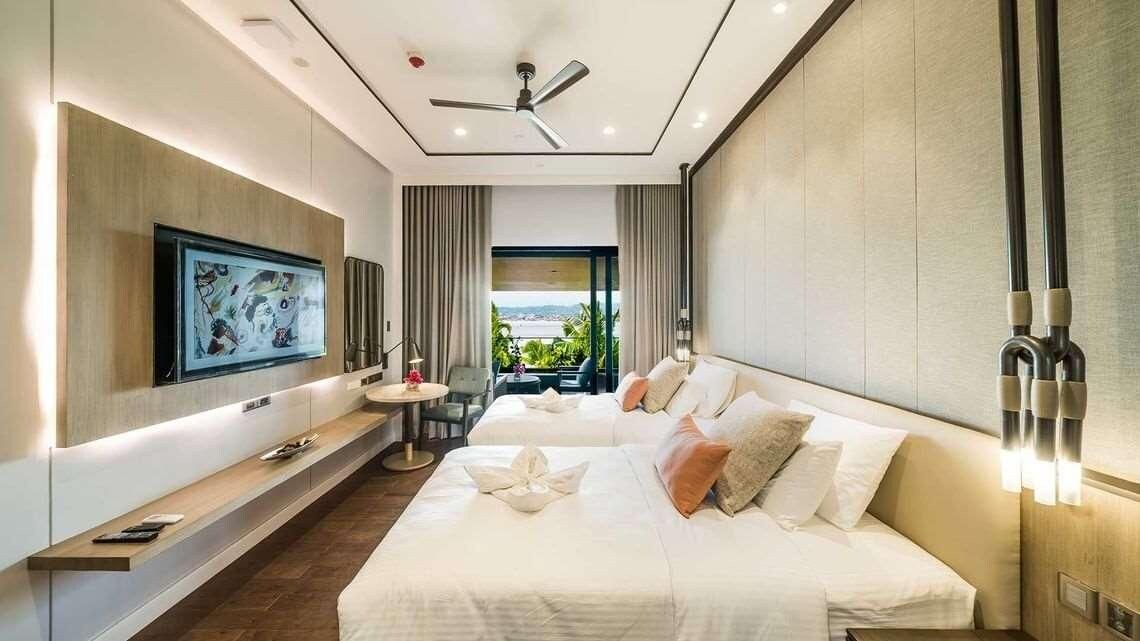 A modern hotel room with a large bed, a TV mounted on the wall, a ceiling fan, and a view of the outdoors.