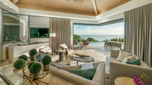 A spacious living area with a modern design, featuring a large sofa, a coffee table, and a TV mounted on the wall. There is a view of the ocean through large windows. - Discovery Samal (Samal)