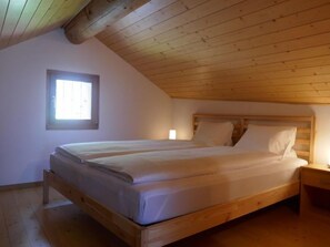 Quarto com estrutura de cama de madeira, duas camas individuais, uma janela com persianas e teto inclinado.