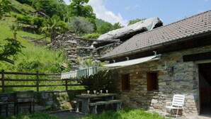 A stone building with a tiled roof, a stone wall, and a wooden fence. - Rustico Cleo by Interhome (Semione)