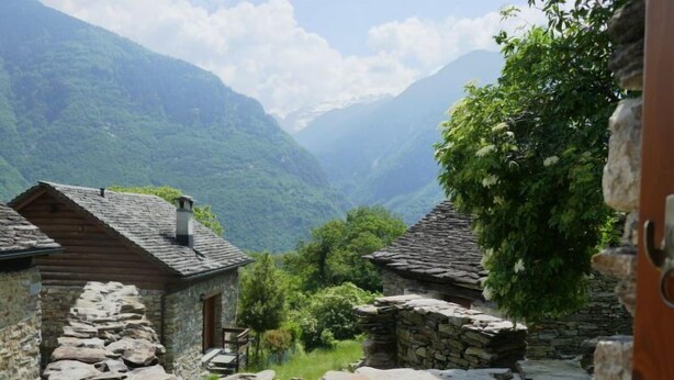 A rustic stone building with a sloped roof, surrounded by lush greenery and mountains in the background. - Rustico Cleo by Interhome (Semione)
