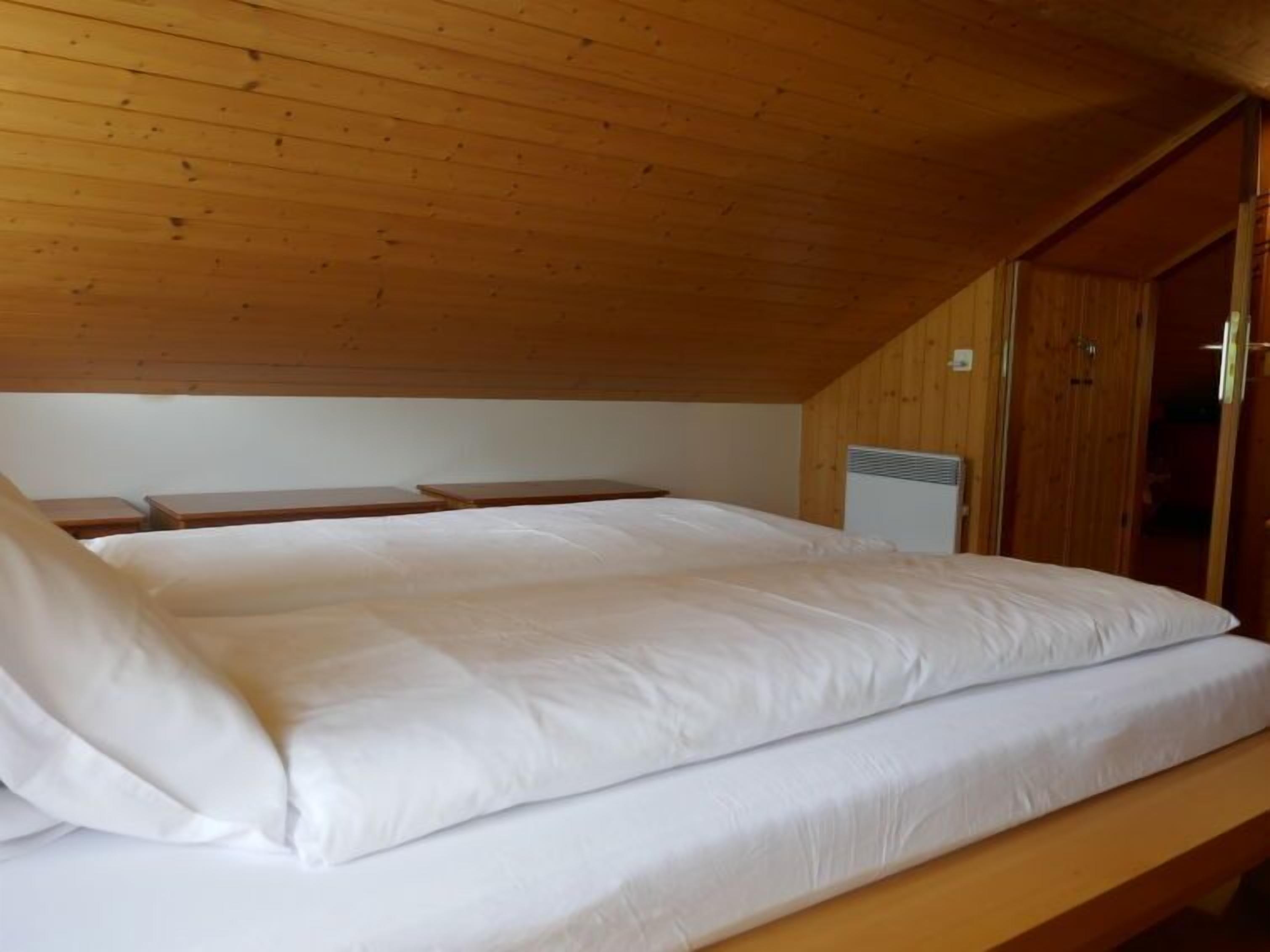 Un lit simple dans une pièce aux murs en bois et au plafond en pente.