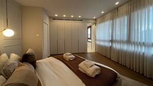 Ett modernt hotellrum med en stor säng, en rymlig klädkammare och utsikt över staden genom fönstret.
