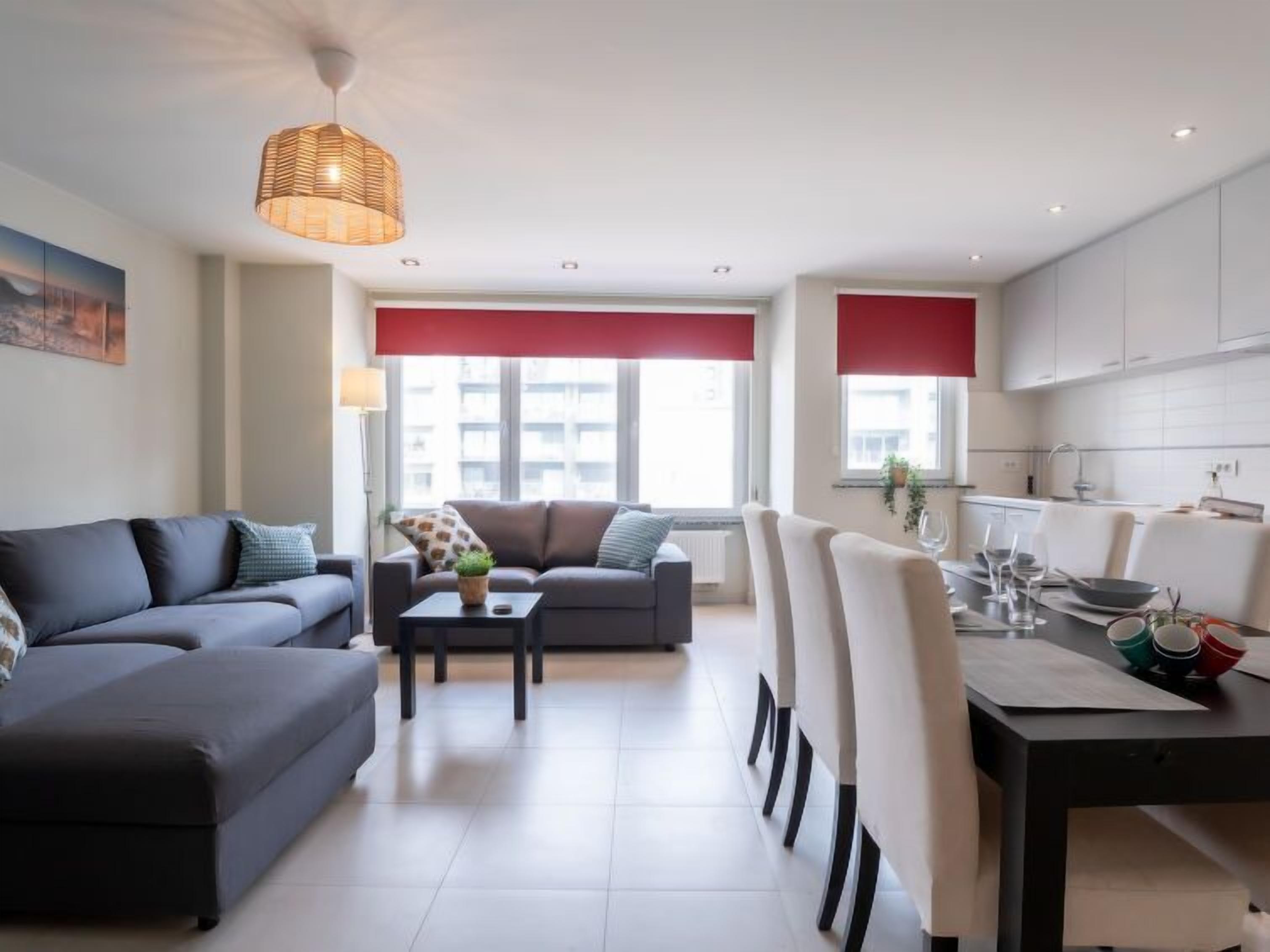 A modern living room with a sofa, a coffee table, and a dining area with chairs and a table set for a meal.