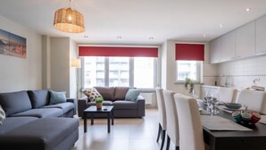 A modern living room with a sofa, a coffee table, and a dining area with chairs and a table set for a meal. - Apartment Andrei by Interhome (Blankenberge)