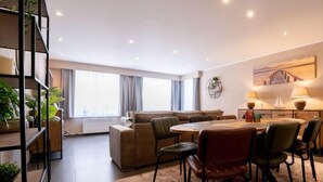 A modern living room with a sofa set, a dining table with chairs, a bookshelf, and a large window with curtains. - Philemon with parking by Interhome (Blankenberge)