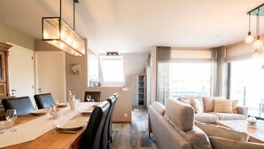Un salon moderne comprenant un canapé, une table à manger et des chaises. On y trouve également un coin cuisine avec des placards et une fenêtre.