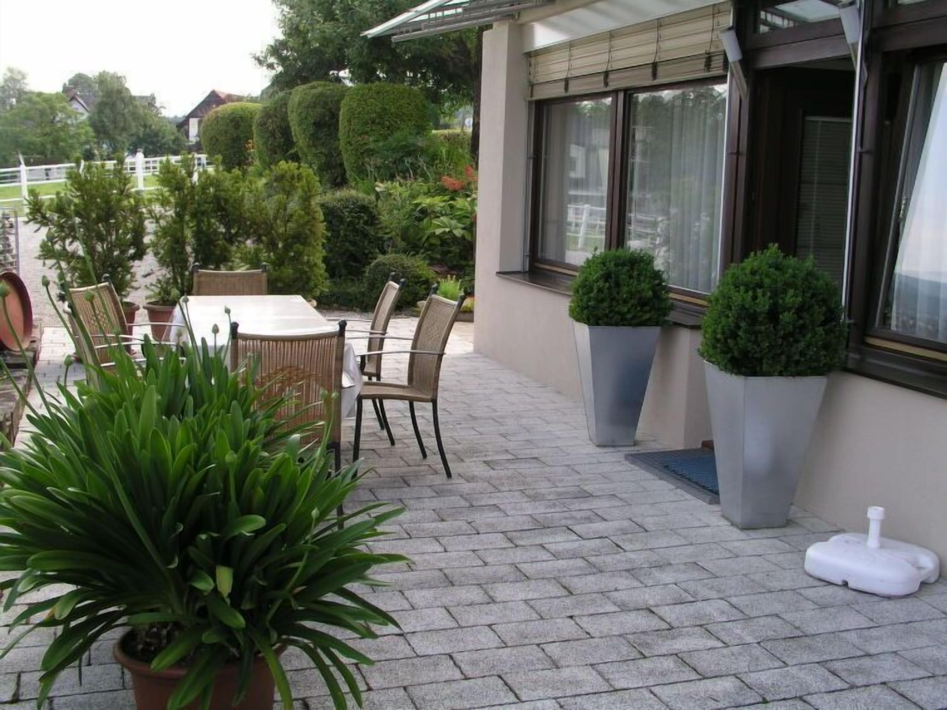 An outdoor patio with a table and chairs, potted plants, and a window with blinds.