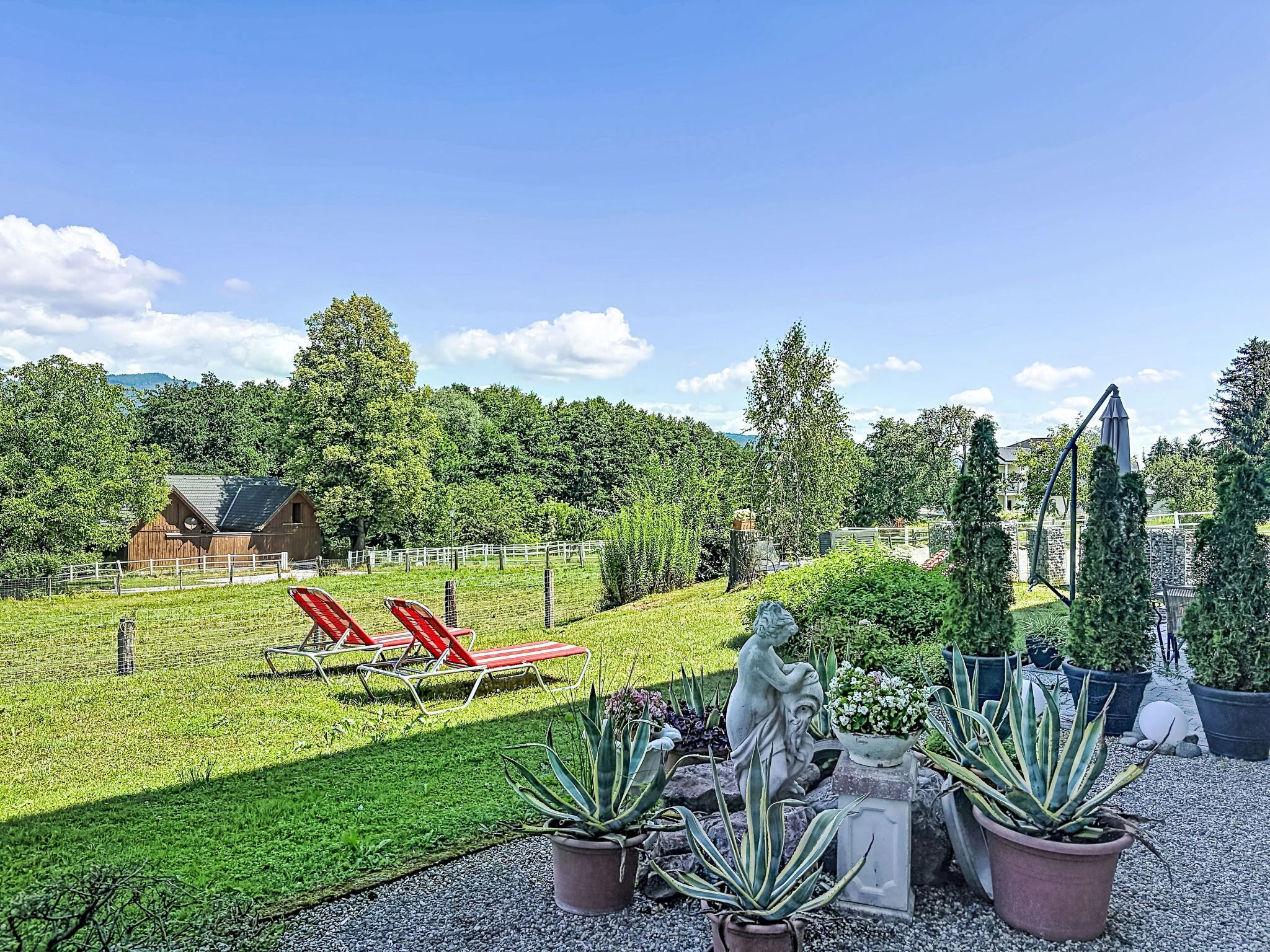 Un jardin avec des fauteuils de relaxation rouges, une statue et des plantes en pot.