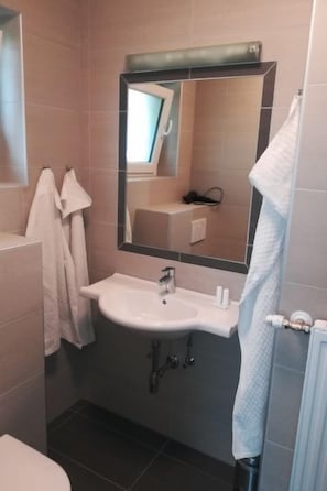 A bathroom with a white sink, a mirror above it, and a towel hanging on the wall. - Apartment Tulpe by Interhome (Velden am Wörthersee)