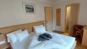 Un letto ben rifatto con lenzuola bianche e asciugamani piegati, una testiera in legno, un quadro incorniciato appeso alla parete e porte in legno.