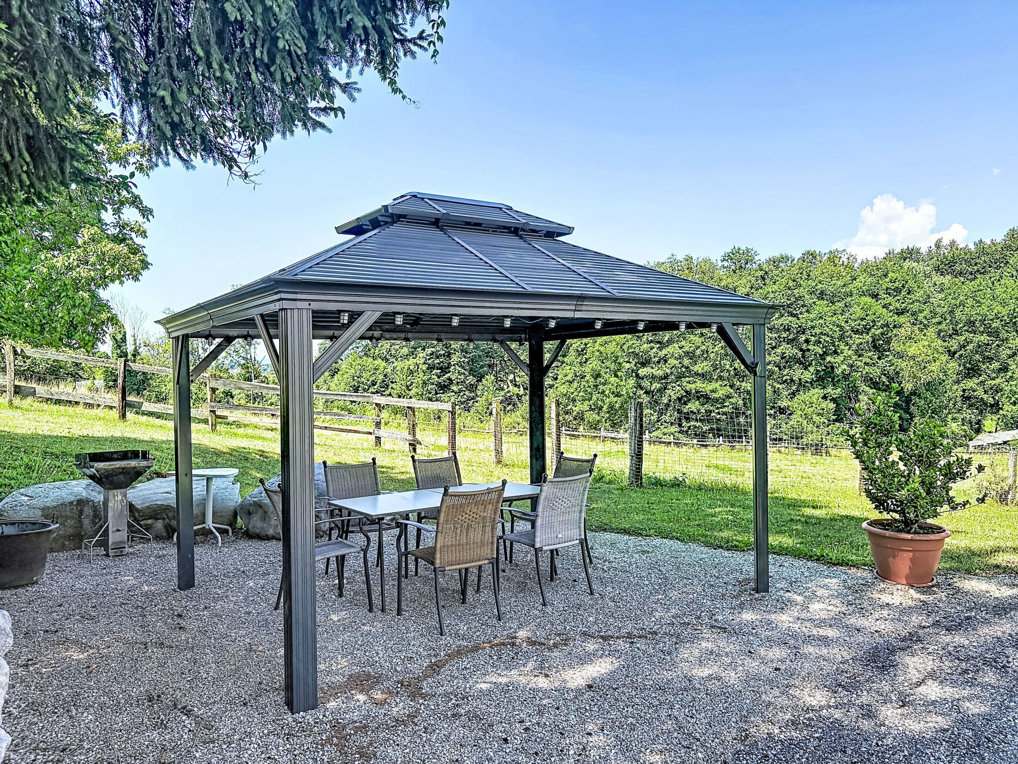 Un kiosque doté d’un toit en métal et d’un sol en gravier, entouré de chaises et d’une table.