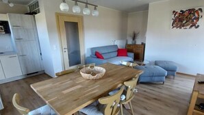 Un soggiorno moderno con tavolo da pranzo in legno, sedie, un divano blu e angolo cottura.