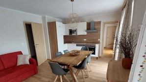Een moderne keuken met witte kasten, een houten eettafel en een rode bank.