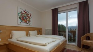 Een hotelkamer met een groot bed, een houten hoofdbord, een rood tapijtbalk en een rieten stoel, met uitzicht op de omgeving via een schuifdeur.'