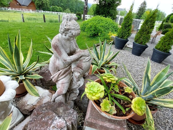 Un giardino con una statua in pietra, piante in vaso e un recinto bianco sullo sfondo.