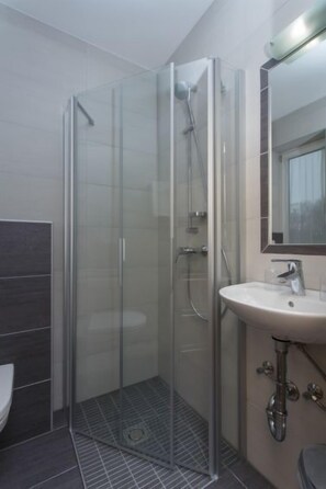 Ein modernes Badezimmer mit einer Duschkabine, einem Waschbecken auf Säule und einem großen Spiegel.