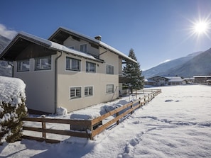 A two-story chalet with a wooden deck and a snow-covered landscape.