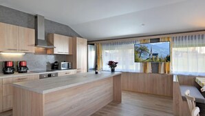 Una cocina moderna con armarios de madera, una isla central y un comedor con vistas a montañas.