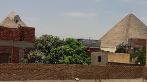 Una estructura piramidal con una antena parabólica en un edificio a la izquierda y un árbol en primer plano.