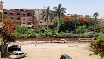 Zona residencial con edificios de varios pisos, una calle de arena y abundante vegetación, incluyendo árboles con flores rojas.