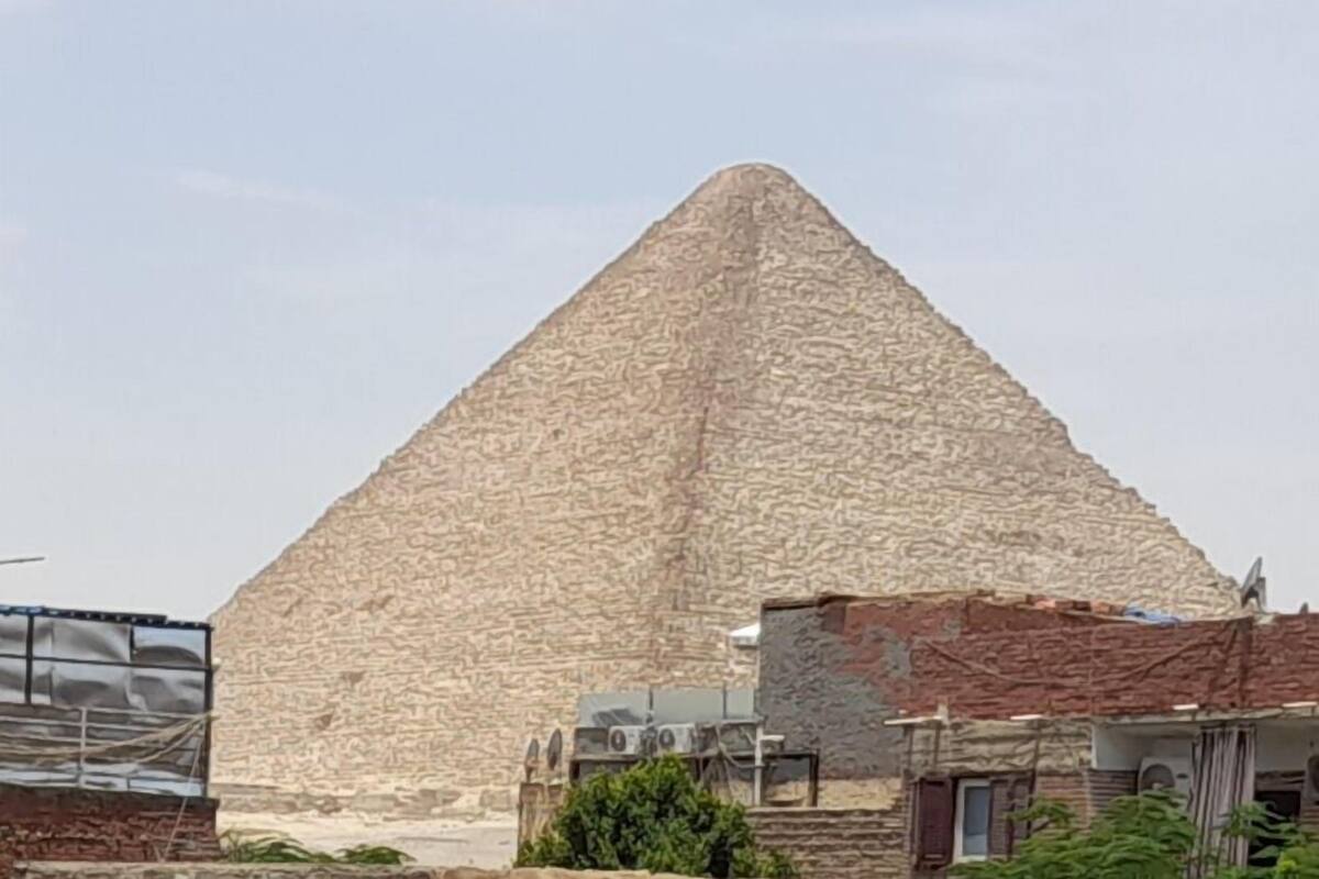 Une grande structure pyramidale en pierre, surmontée d’un sommet plat, entourée de bâtiments à l’architecture moderne et traditionnelle.