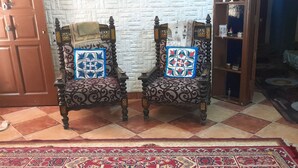 Una habitación con dos sillones ornamentados con cojines estampados, un aparador de madera y una alfombra roja con diseño.