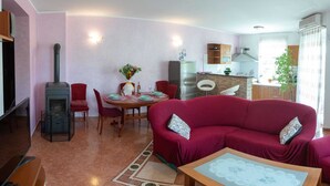 A living room with a red sofa, a dining table set for four, a kitchen area with a stove, and a large window. - KATA Two-Bedroom Apartment with Balcony (Rovinj)