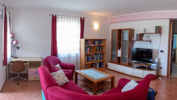 Ein Wohnzimmer mit Schreibtisch, zwei roten Sofas, einem Bücherregal, einem Fernseher und einem Kleiderschrank.