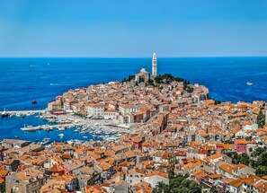 Une ville côtière dotée d’un imposant beffroi, de bâtiments aux toits couverts de tuiles rouges et d’un port de plaisance où sont amarrés des bateaux.