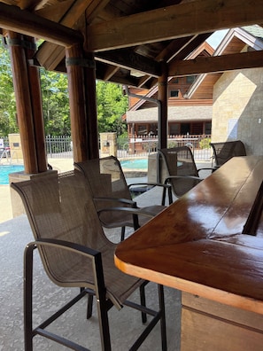 Une terrasse extérieure avec des tables et des chaises en bois, une piscine et un bâtiment en pierre en arrière-plan.