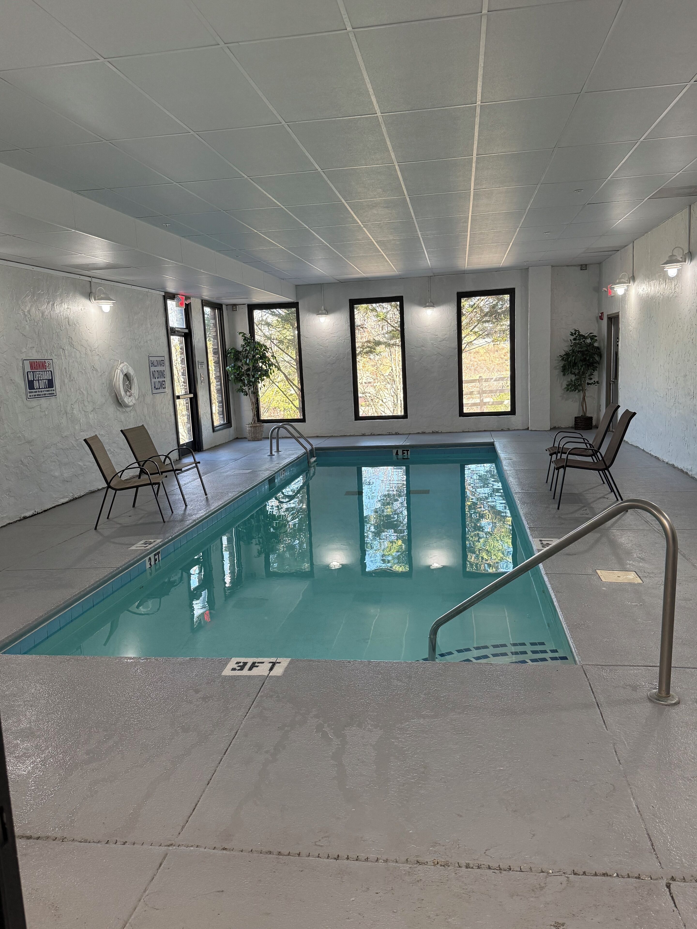 An indoor swimming pool with clear water, surrounded by walls with windows and a ceiling with grid-like panels.