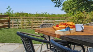 An outdoor dining area with a wooden table, wicker chairs, and a view of a green lawn and wooden fence. - No. 4 Squirrels Nest-UK44305 (Great Witchingham)
