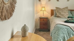 A bedroom with a bed, a nightstand with a lamp, a wall mirror, and a decorative wall piece. - No. 4 Squirrels Nest-UK44305 (Great Witchingham)