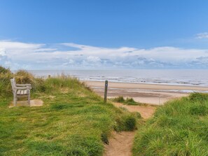 A beach path with a bench and a signpost.