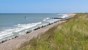 A coastal walkway with a concrete path, grassy areas, and a clear view of the ocean. - No. 4 Squirrels Nest-UK44305 (Great Witchingham)