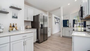 Una cocina moderna con muebles blancos, un refrigerador de acero inoxidable y una encimera con un tostador y botellas de azúcar.