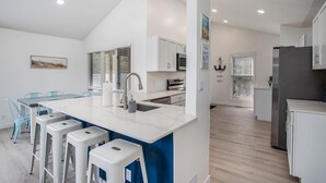 Una cocina moderna con armarios blancos, una isla central con taburetes y una zona de comedor con sillas azules.