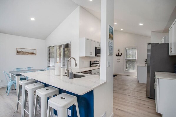A modern kitchen with white cabinetry, a central island with stools, and a dining area with blue chairs.