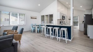 Una cocina moderna con una isla central, taburetes de bar y una zona de estar con sillas.