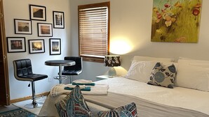 Una camera da letto con un letto, una sedia, un tavolo e un quadro appeso al muro.