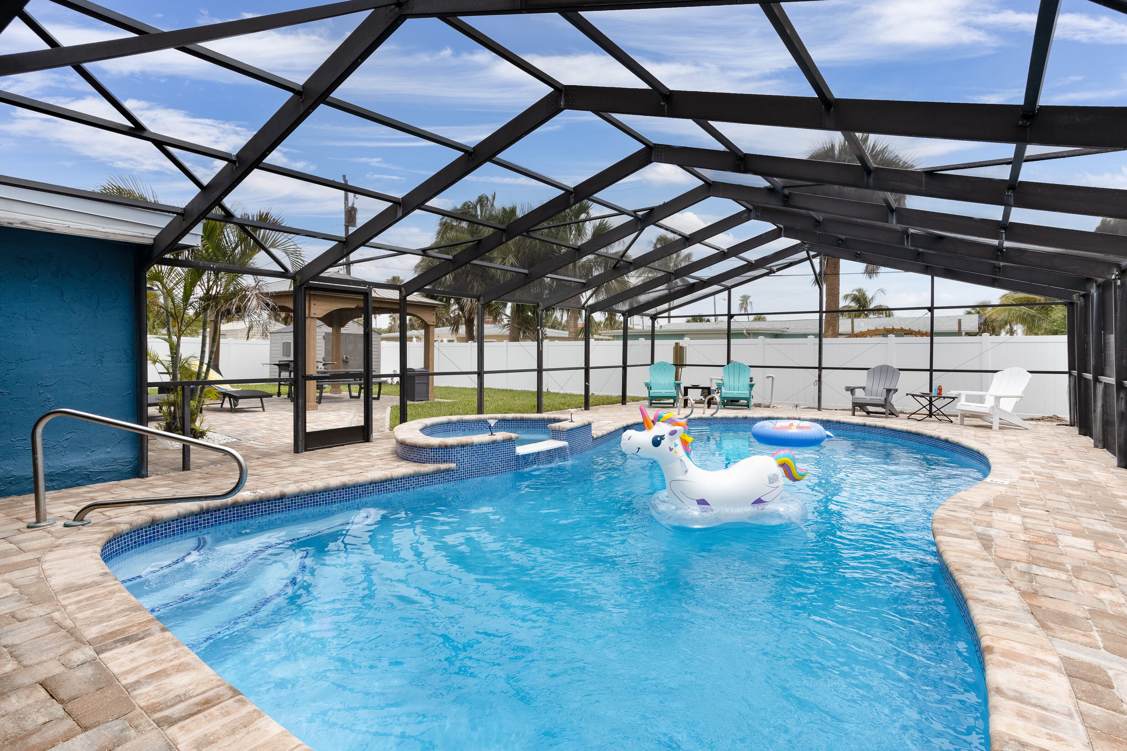 An indoor swimming pool with a glass ceiling, a unicorn float, and a brick pool edge.