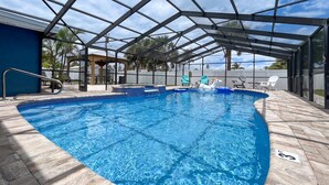 A covered outdoor swimming pool with a clear blue water, surrounded by a tiled deck and a metal roof structure. - Beach Getaway on Cocoa Beach (Cocoa Beach)