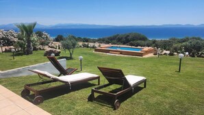 A poolside area with two lounge chairs, a small pool, and a view of the sea and mountains.