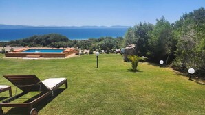 A pool with a clear view of the sea, surrounded by a grassy area and trees.