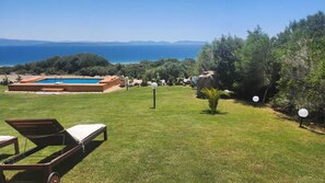 Una piscina con vistas despejadas al mar, rodeada de césped y árboles.