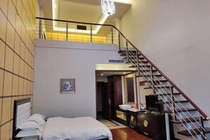 A bedroom with a bed, a dresser, a mirror, and a staircase.