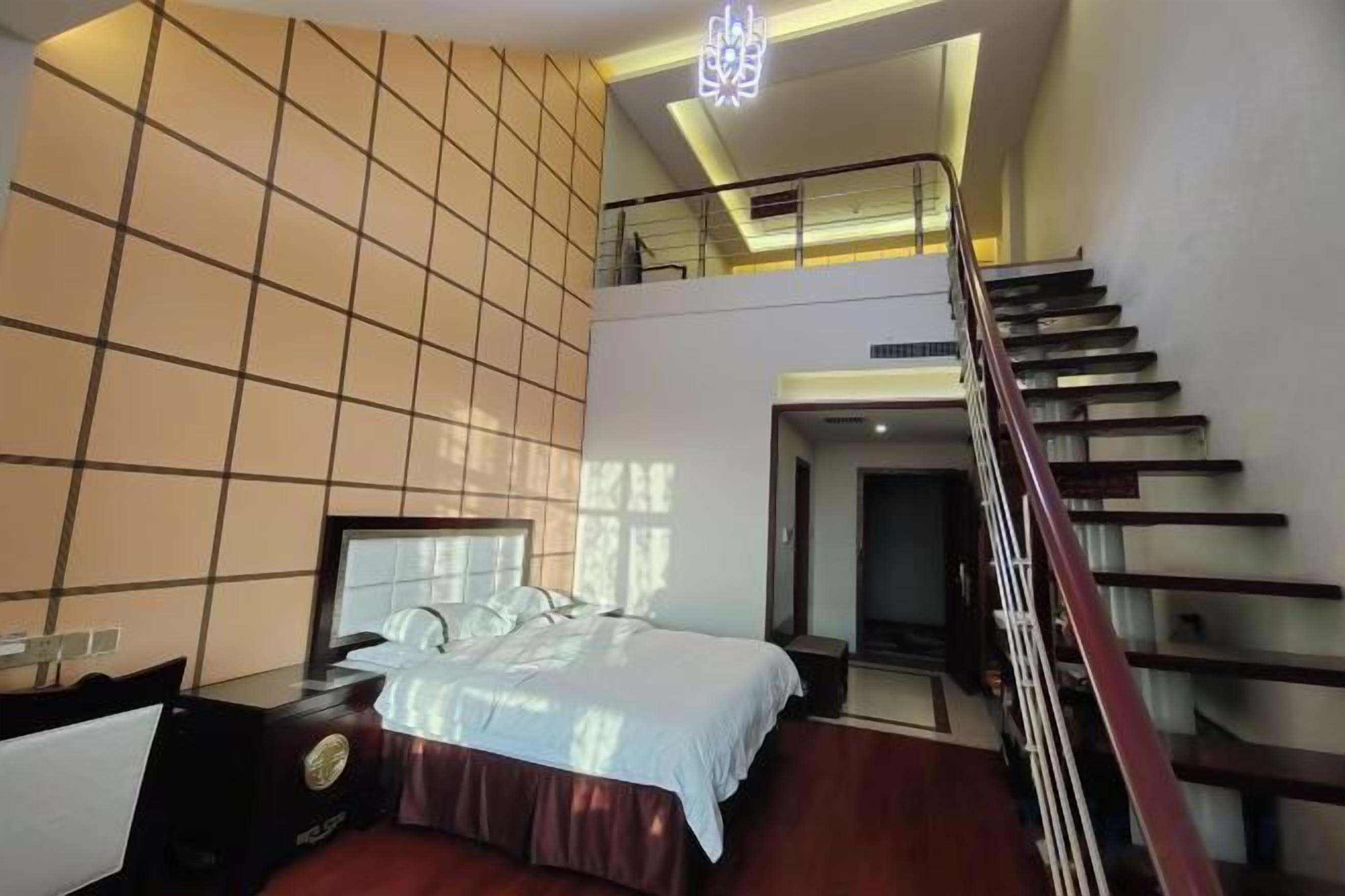 A modern hotel room with a bed, a nightstand, a desk, and a staircase.