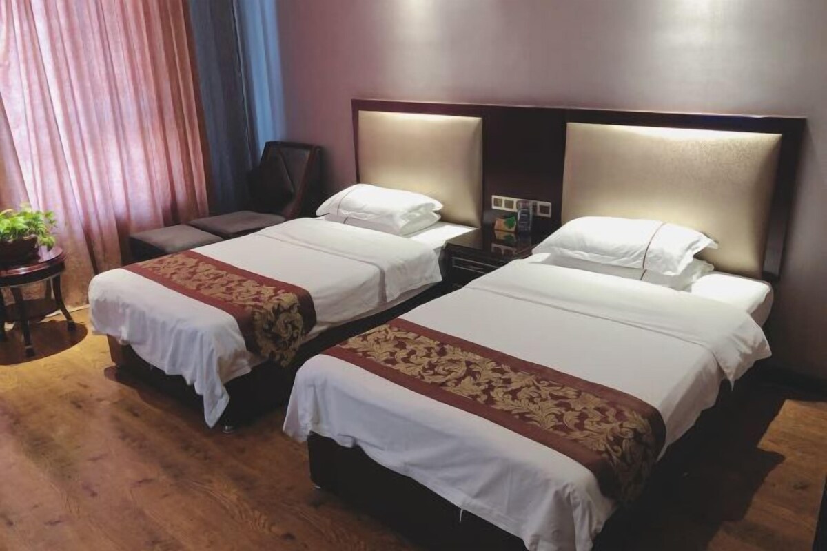 A hotel room with two beds, a wooden floor, a desk, and a chair.