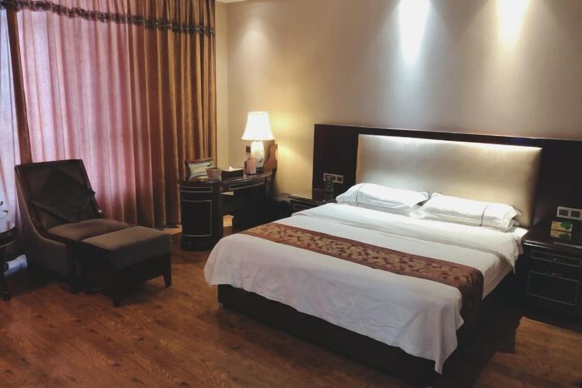 A hotel room with a large bed, a chair, a nightstand, a lamp, and a curtain.